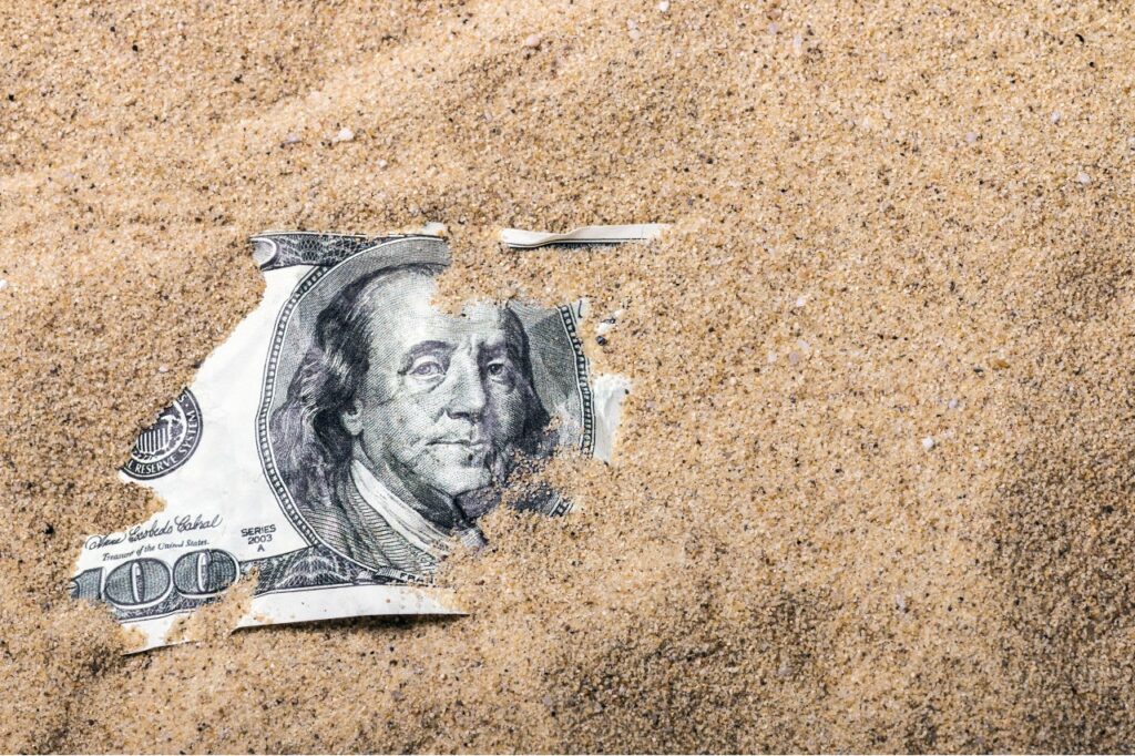 $100 bill half-buried in beach sand