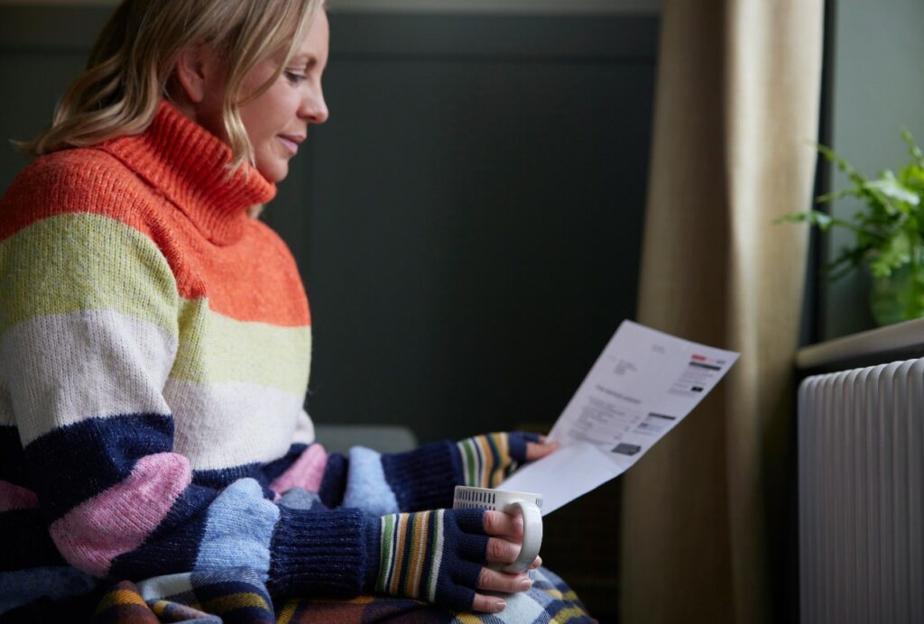 Cold Wisconsin woman in sweater and gloves looking at expensive energy bill